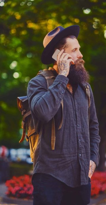 Bearded tattooed traveller male using a smartphone in a town.